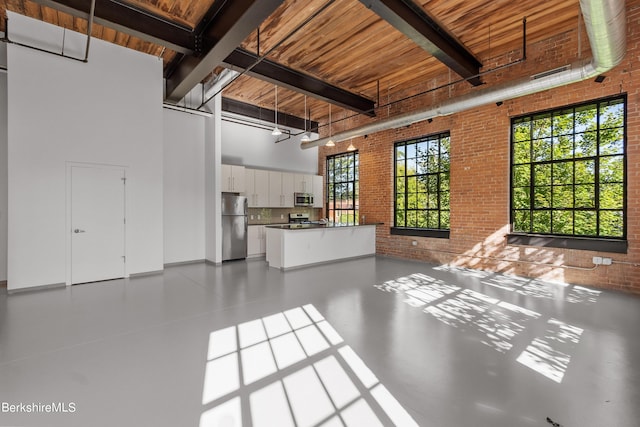 unfurnished living room with beam ceiling, wooden ceiling, a towering ceiling, and brick wall