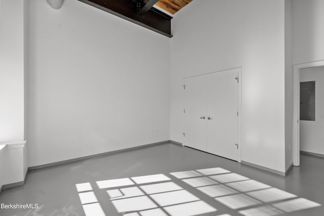 unfurnished bedroom featuring concrete floors, a towering ceiling, electric panel, and a closet