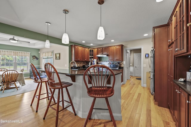 200 Easthampton Rd, Westhampton, MA 01027 - kitchen with stainless steel microwave, a breakfast bar area, under cabinet range hood, glass insert cabinets, and decorative backsplash