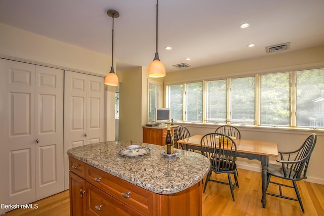 770 Summer St Unit 5D, Lee, MA 01238 - kitchen with brown cabinets, light stone counters, a kitchen island, light wood-style flooring, and pendant lighting