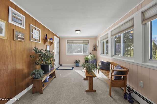 sitting room with a baseboard heating unit, carpet floors, ornamental molding, and wood walls