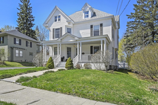 view of front of home featuring roof with shingles, covered porch, and a front yard