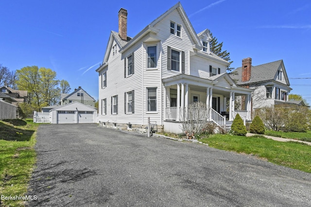 view of front of house with covered porch, a chimney, an outdoor structure, and a detached garage