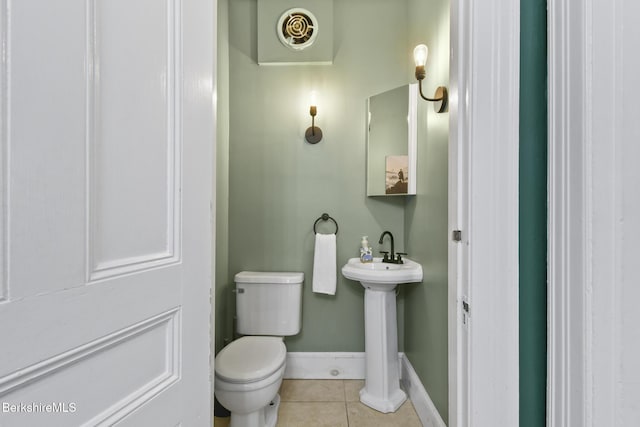 half bath with baseboards, a sink, tile patterned floors, and toilet
