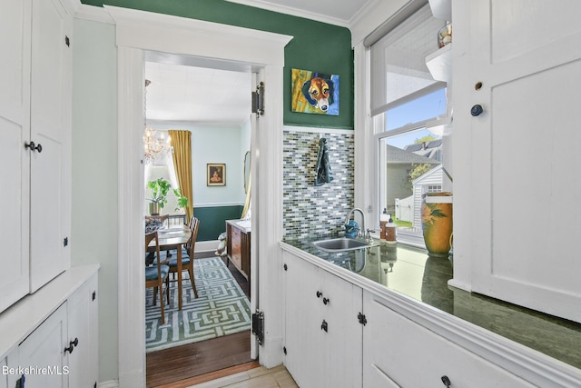 doorway to outside with a sink, baseboards, light wood finished floors, a notable chandelier, and ornamental molding
