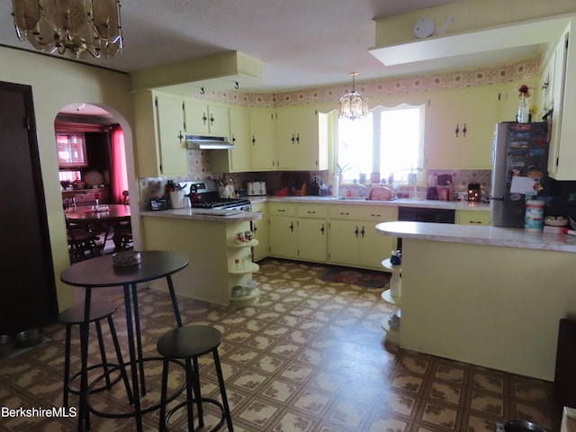 kitchen with under cabinet range hood, light floors, appliances with stainless steel finishes, arched walkways, and a notable chandelier