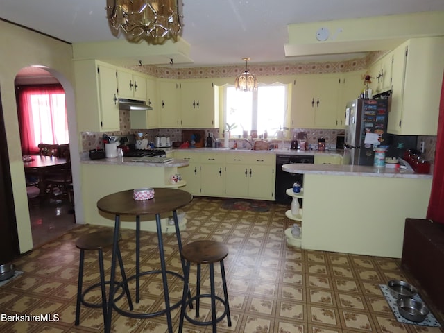 kitchen featuring under cabinet range hood, arched walkways, black dishwasher, and light floors