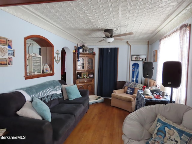 living area with a ceiling fan, an ornate ceiling, wood finished floors, arched walkways, and crown molding