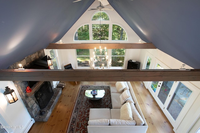 living room with baseboard heating, a stone fireplace, ceiling fan with notable chandelier, and vaulted ceiling