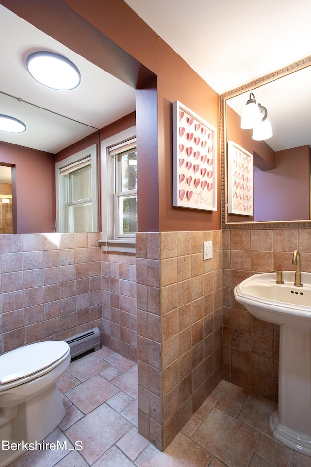 bathroom with toilet, sink, tile walls, and a baseboard heating unit