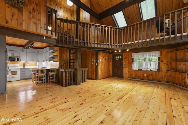 377 Highland Way, Sandisfield, MA 01255 - unfurnished living room featuring light wood-type flooring, a towering ceiling, wood walls, a baseboard radiator, and a skylight