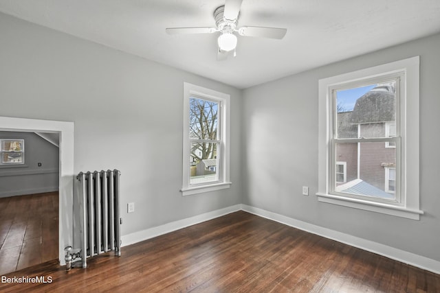 spare room featuring baseboards, a healthy amount of sunlight, dark wood-style flooring, and radiator heating unit