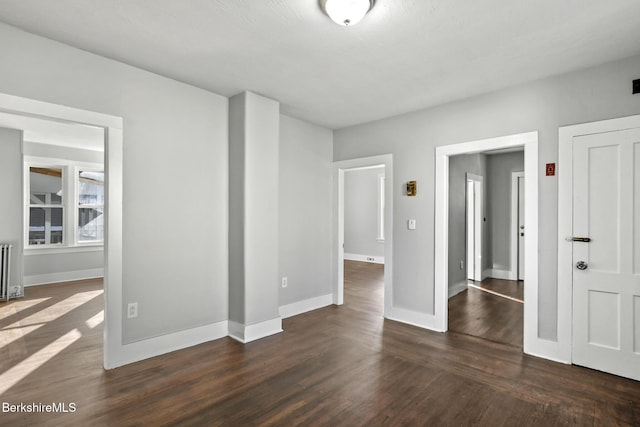 empty room featuring radiator, wood finished floors, and baseboards