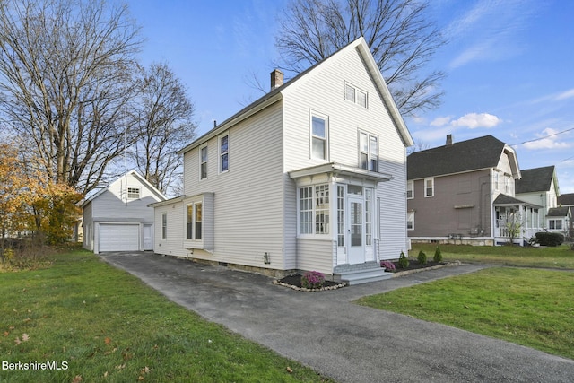 view of front of house with a detached garage, aphalt driveway, entry steps, a chimney, and an outbuilding