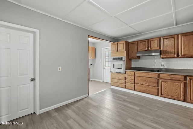 kitchen featuring under cabinet range hood, tasteful backsplash, light wood-style floors, stainless steel oven, and black electric stovetop