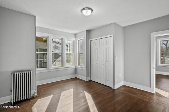 unfurnished bedroom featuring radiator, wood finished floors, baseboards, and a closet