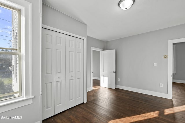 unfurnished bedroom featuring a closet, baseboards, and dark wood-style flooring