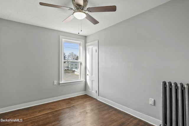 spare room with baseboards, radiator, dark wood finished floors, and a ceiling fan