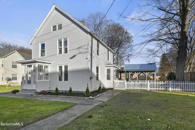 view of front of house with fence, a front yard, metal roof, a chimney, and a sunroom