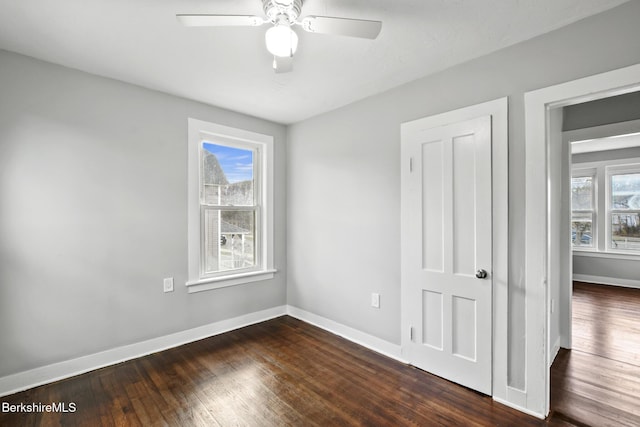 unfurnished room with a wealth of natural light, baseboards, dark wood finished floors, and a ceiling fan