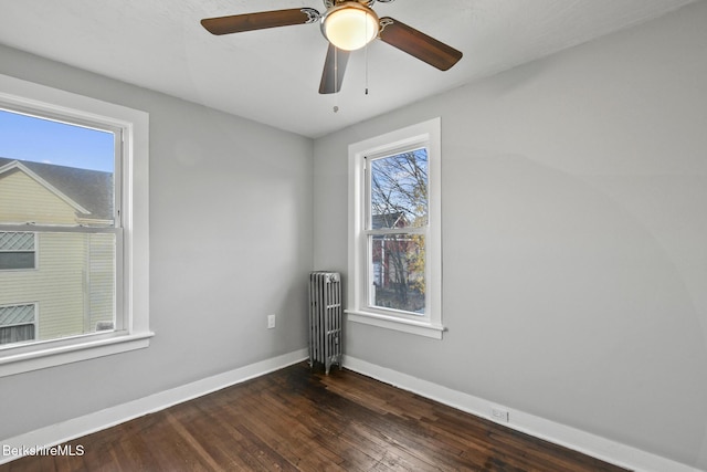 unfurnished room featuring baseboards, a ceiling fan, dark wood-style floors, and radiator heating unit