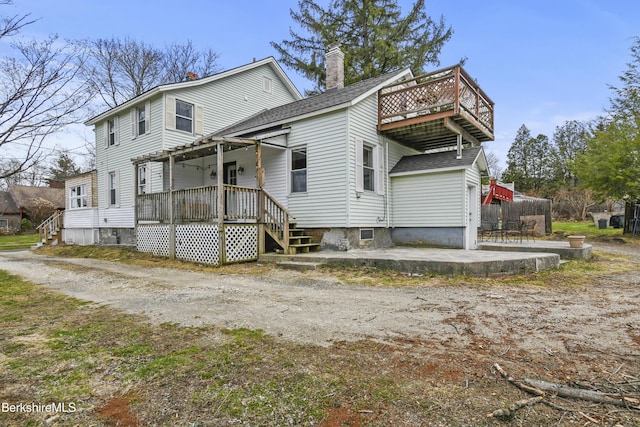 back of house featuring roof with shingles, a patio area, a wooden deck, and a chimney