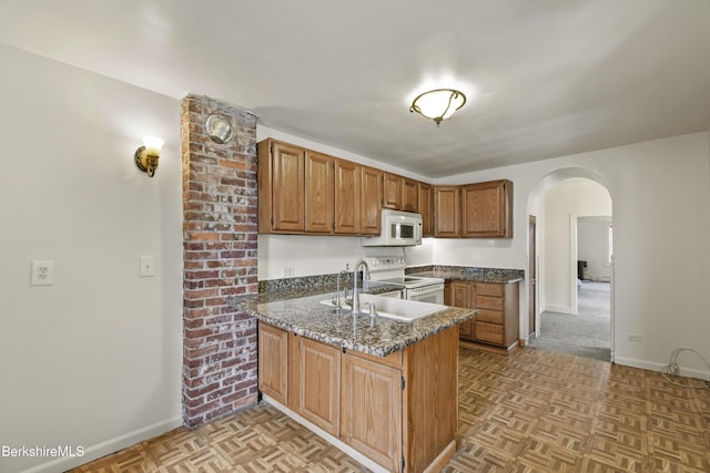 kitchen with brown cabinets, baseboards, arched walkways, white appliances, and a peninsula