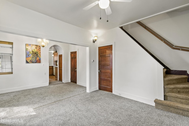unfurnished living room with carpet flooring, stairway, baseboards, arched walkways, and a ceiling fan
