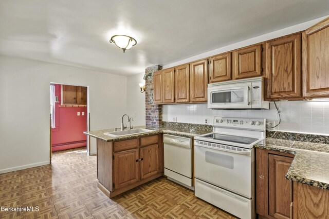 kitchen featuring white appliances, a peninsula, backsplash, and a sink