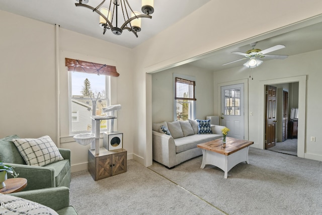 living room featuring light colored carpet, baseboards, ceiling fan with notable chandelier, and radiator