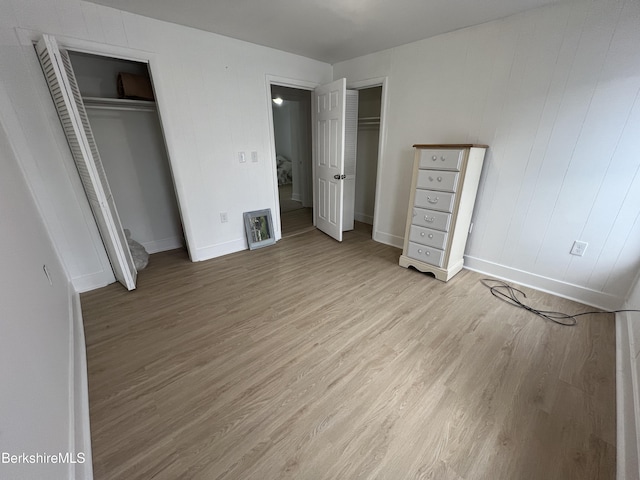 unfurnished bedroom featuring light wood-type flooring, multiple closets, and baseboards