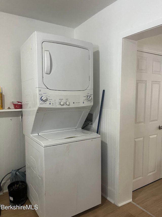 laundry room featuring a wainscoted wall, stacked washer and dryer, wood finished floors, and laundry area