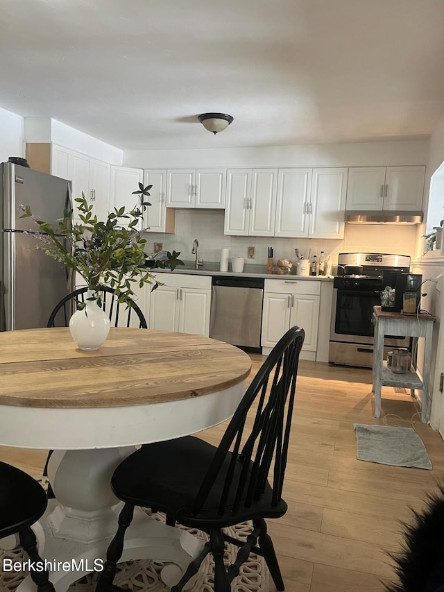 kitchen with white cabinetry, under cabinet range hood, appliances with stainless steel finishes, and a sink