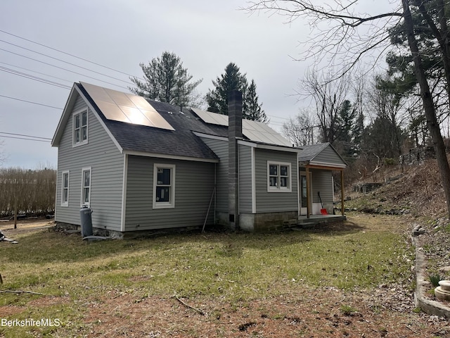 back of property featuring a chimney, a lawn, roof mounted solar panels, and a shingled roof