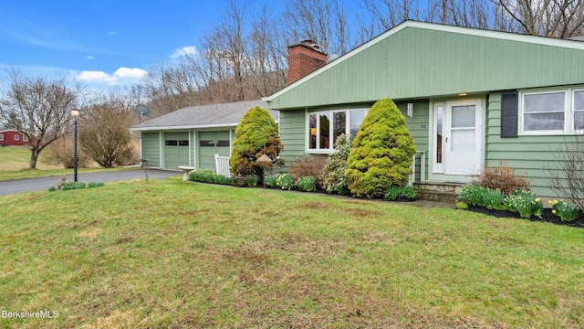 view of front of home featuring a chimney, a garage, driveway, and a front lawn