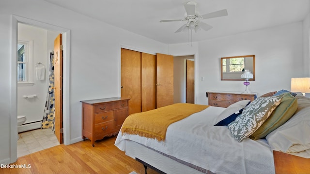 bedroom with ceiling fan, ensuite bathroom, light wood-style flooring, a closet, and a baseboard radiator