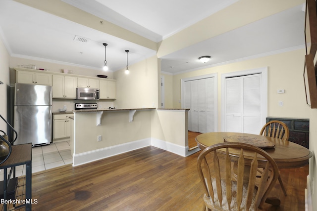 kitchen with pendant lighting, a breakfast bar area, ornamental molding, kitchen peninsula, and stainless steel appliances