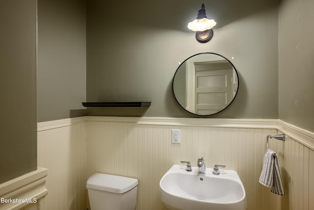bathroom featuring a sink, toilet, and a wainscoted wall