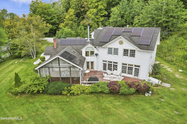 back of house featuring a sunroom, solar panels, a patio, and a lawn