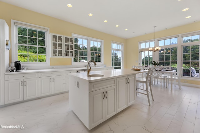 kitchen with sink, hanging light fixtures, an inviting chandelier, a center island with sink, and white cabinets