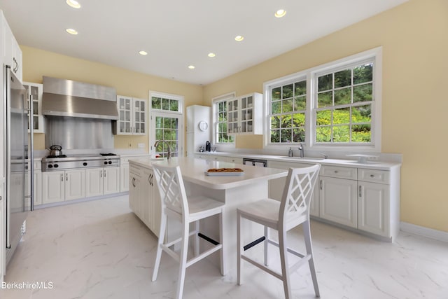 kitchen featuring white cabinets, wall chimney range hood, sink, a kitchen island, and stainless steel gas cooktop