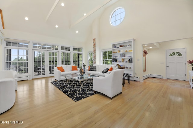 living room with a towering ceiling, baseboard heating, beamed ceiling, light hardwood / wood-style floors, and plenty of natural light