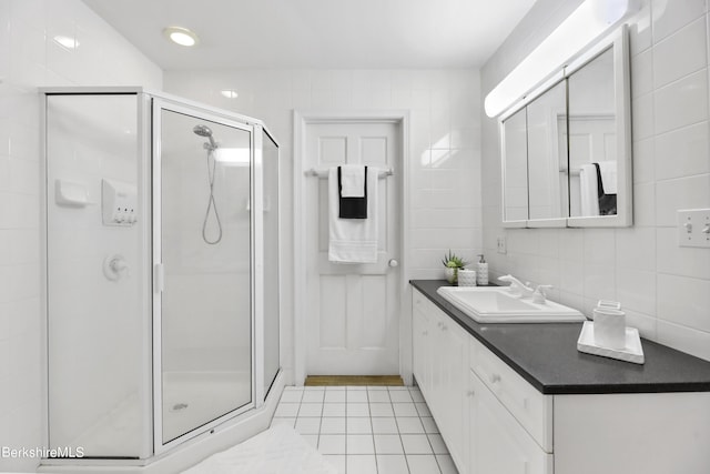 bathroom with tile patterned floors, a shower with door, vanity, and tile walls