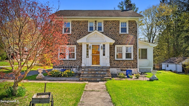 colonial-style house featuring a chimney, brick siding, a front yard, and entry steps
