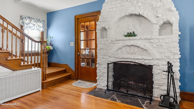 living area with radiator heating unit, a fireplace, stairs, and wood finished floors