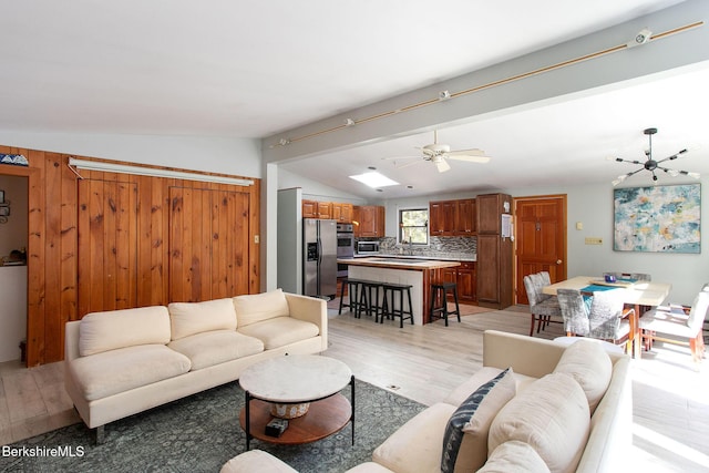 living area featuring ceiling fan with notable chandelier, light wood-style floors, and vaulted ceiling