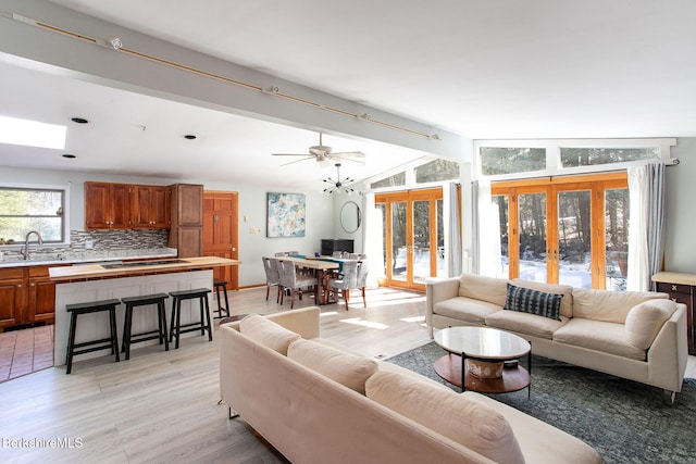 living room featuring lofted ceiling with beams, french doors, and light wood-style flooring