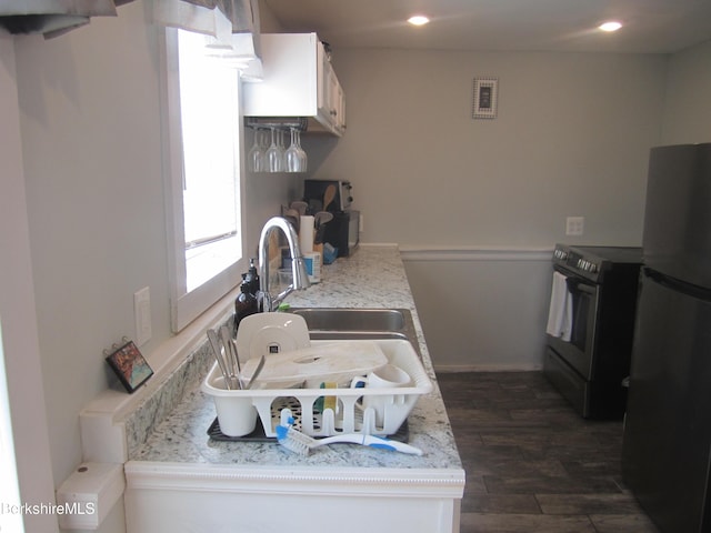 kitchen with black electric range oven, light stone counters, fridge, dark hardwood / wood-style flooring, and white cabinetry