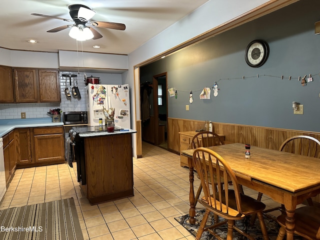 kitchen featuring ceiling fan, white fridge with ice dispenser, wood walls, decorative backsplash, and a kitchen island