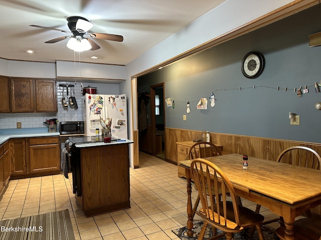 kitchen featuring ceiling fan, a kitchen island, white refrigerator with ice dispenser, decorative backsplash, and light tile patterned floors